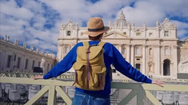Şapkalı ve sırt çantalı bir turist kız Vatikan 'daki Aziz Peters Bazilikası' nın önünde duruyor..