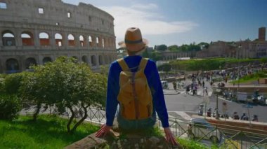 Şapkalı ve sırt çantalı bir kız Roma 'daki Colosseum' un arka planında Roma 'nın ünlü simgesine bakıyor. İtalya.