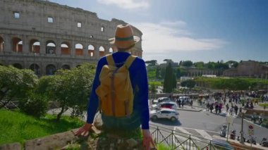 Şapkalı ve sırt çantalı bir kız, güneşli bir günde Roma 'daki Colosseum' a bakıyor..