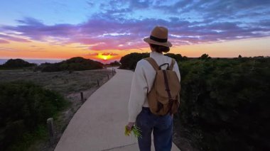 Şapkalı ve sırt çantalı bir kız Ponta de Piedade 'deki bir uçurumun kenarına okyanusun en güzel gün batımını görmeye gider, Portekiz..