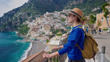 Şapkalı ve sırt çantalı bir kız turist Amalfi kıyısındaki ünlü İtalyan turist kasabası Positano 'nun güzelliğine hayran. İtalya.