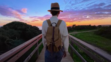 Şapkalı ve sırt çantalı bir kız Ponta de Piedade 'deki bir uçurumun kenarına okyanusun en güzel gün batımını görmeye gider, Portekiz..