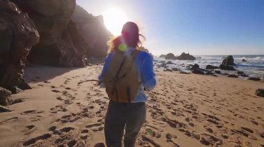 Sırt çantalı mutlu kız turist ıssız Ursa sahilinde koşuyor. Portekiz.