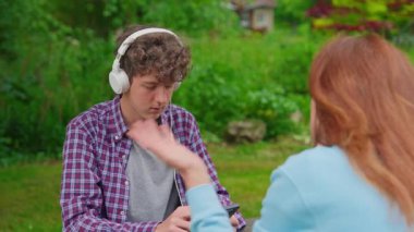 Annem onu dinlemek istemeyen bir ergenle konuşup bazı sorunları çözmeye çalışıyor. Ergen, annesini dinlemekten kaçınıyor. Kulaklıkla modern aletlerle oturuyor..