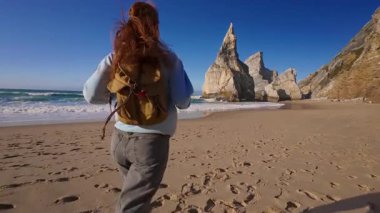 Sırt çantalı mutlu kız turist ıssız Ursa sahillerinde koşuyor ve okyanusun tadını çıkarıyor. Portekiz.