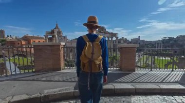 Şapkalı ve sırt çantalı turist kadın Roma Forumu 'ndaki Antik Roma Sütunları' nın manzaralarını düşünüyor. İtalya. Arka planda yürüyen bir kız manzarası manzarası.