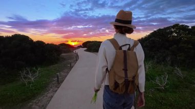 Şapkalı ve sırt çantalı bir kız Ponta de Piedade 'deki bir uçurumun kenarına okyanusun en güzel gün batımını görmeye gider, Portekiz..