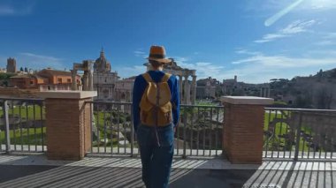 Şapkalı ve sırt çantalı turist kadın Roma Forumu 'ndaki Antik Roma Sütunları' nın manzaralarını düşünüyor. İtalya. Arka planda yürüyen bir kız manzarası manzarası.