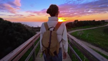 Şapkalı ve sırt çantalı bir kız Ponta de Piedade 'deki bir uçurumun kenarına okyanusun en güzel gün batımını görmeye gider, Portekiz..