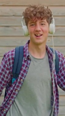 Dikey video. Genç, mutlu, kıvırcık kız kulaklıklarla dans ediyor, komik dans figürleriyle eğleniyor, sokaklarda özgürce yürüyor..