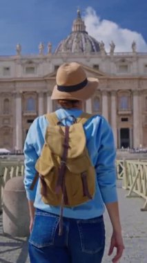 Şapkalı ve sırt çantalı bir turist kız Vatikan, İtalya 'daki ikonik St. Peters Meydanı' na hayranlıkla bakıyor. 29.04.2025.