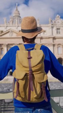 Şapkalı ve sırt çantalı bir turist kız Vatikan 'daki Aziz Peters Bazilikası' nın önünde duruyor..