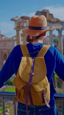 Şapkalı ve sırt çantalı turist kadın Roma Forumu 'ndaki Antik Roma Sütunları' nın manzaralarını düşünüyor. İtalya. Arka planda yürüyen bir kız manzarası manzarası.