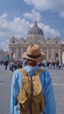 Şapkalı ve sırt çantalı bir turist kız Vatikan, İtalya 'daki ikonik St. Peters Meydanı' na hayranlıkla bakıyor. 29.04.2025.