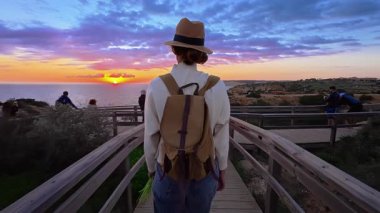 Şapkalı ve sırt çantalı bir kız Ponta de Piedade 'deki bir uçurumun kenarına okyanusun en güzel gün batımını görmeye gider, Portekiz..
