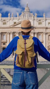 Şapkalı ve sırt çantalı bir turist kız Vatikan 'daki Aziz Peters Bazilikası' nın önünde duruyor..