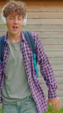 Dikey video. Genç, mutlu, kıvırcık kız kulaklıklarla dans ediyor, komik dans figürleriyle eğleniyor, sokaklarda özgürce yürüyor..