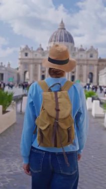 Şapkalı ve sırt çantalı bir turist kız Vatikan, İtalya 'daki ikonik St. Peters Meydanı' na hayranlıkla bakıyor. 29.04.2025.