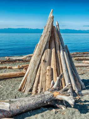 Driftwood logs have been piled up into a simple pyramid form to create a wooden teepee shelter.
