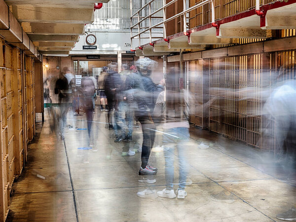 A long exposure view of a corridor in the historic Alcatraz Federal Penitentiary shows the ghostly images of people walking.