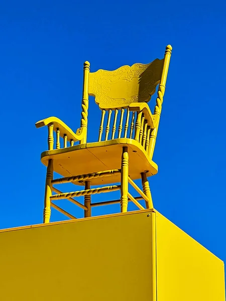 Complementary colors are provided with a bright yellow chair on a pedestal contrasted against a blue sky.