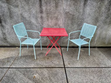 Açık hava mobilyaları, kırmızı masa ve mavi sandalyeler beton bir avluya renk verir aksi takdirde tatsız olurdu..
