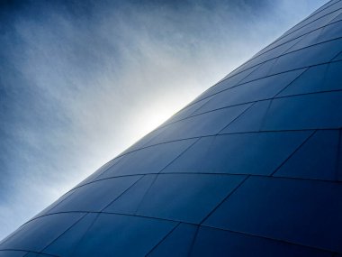 Modern bir binanın dış yüzeyi tarafından oluşturulan ufuktan yükselen çok hafif bir bulutun içinden güneşin parlaması..