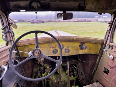 Direksiyona ve eski, paslı bir kamyonun ön camına yakın çekim görüntüsü uzaktaki hurda araçlara ait..