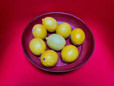 Koyu kırmızı masa örtüsü üzerinde kestane rengi bir kâse ile sekiz parlak sarı limon kontrastı.