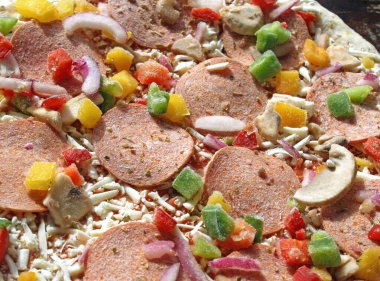 Frozen pizza before cooking.  Toppings include pepperoni, diced red, yellow and green peppers, mushrooms, onions and shredded mozzarella cheese