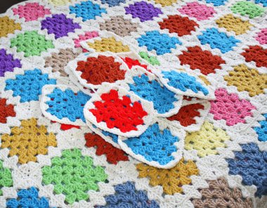 Tamamlanmış battaniyenin yüzeyinde, birçok kareye katıldıktan sonra bir araya getirilmiş renkli el yapımı tığ işi büyükanne kareleri var.