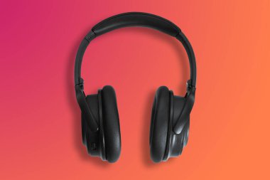 Bilgisayar kulaklıkları. Turuncu arka planda siyah kulaklıklar. Müzik dinleme, ses yaratma, müzik konsepti. Bilgisayar işi, soyutlama ve minimalist stil.