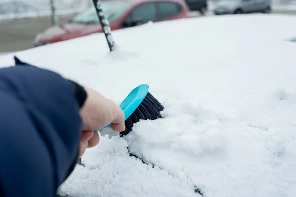 Brush snow removal. The concept of clearing the car from snow, the beginning of winter for motorists, a sudden attack of winter. Sweeping snow off the car.