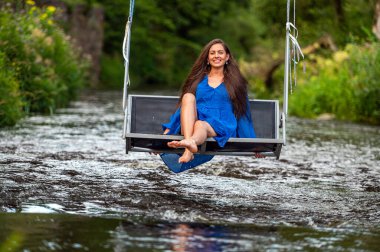 a smiling young woman swings on a rope swing across a fast-flowing river