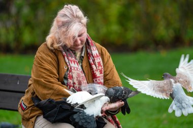Riga, Letonya - 4 Kasım 2022: Bir bankta güvercinleri elleriyle besleyen kadın
