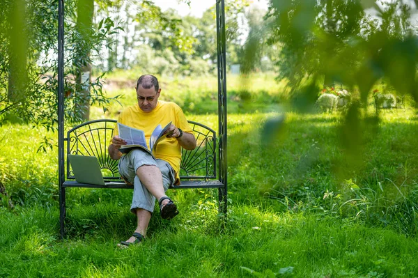 stock image Mature man with laptop and documents working outside in garden, green home office concept.