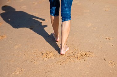 Güneşli bir günde, plajda çıplak ayakla yürüyen bir kadın. Arka manzara, yakın plan.