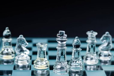 clear glass chess figures arranged in a row reflecting in glass chessboard. Isolated on black