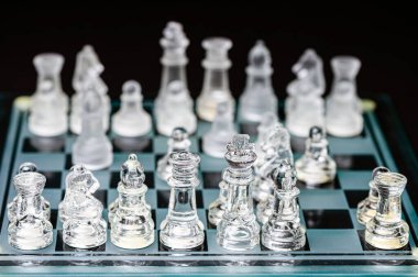 clear glass, transparent chess pieces on a checkerboard, selective focus, closeup, isolated on black