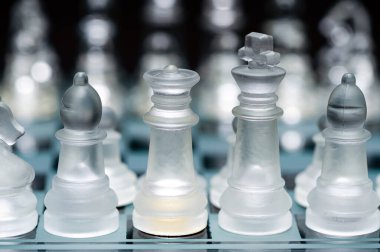 clear glass, transparent chess pieces on a checkerboard, selective focus, closeup, isolated on black