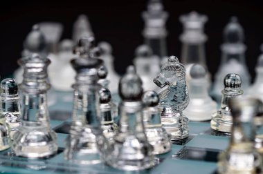 clear glass, transparent chess pieces on a checkerboard, selective focus, closeup, isolated on black