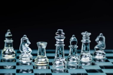 clear glass chess figures arranged in a row reflecting in glass chessboard. Isolated on black