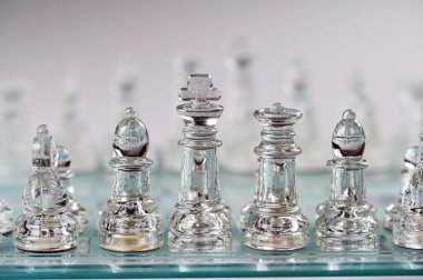 clear glass, transparent chess pieces on a checkerboard, selective focus, closeup, isolated on light