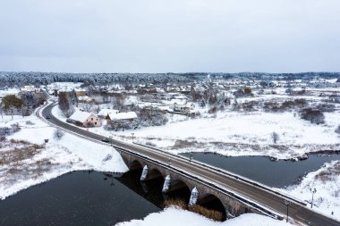 Karlı bir kış gününde Abava nehri üzerinde kemerleri olan eski bir taş köprü, Kandava, hava manzaralı.