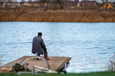 Nehir kenarındaki ahşap köprüde olta kamışı tutan balıkçı, seçici odak, arka görüş.