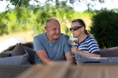 Mutlu orta yaşlı bir çift bahçede dinleniyor ve ferahlatıcı kokteyller içiyor.