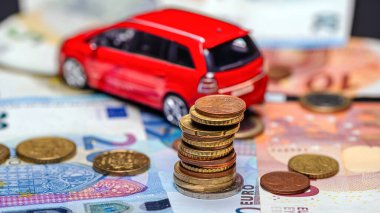 Tower with euro coins on the background of banknotes and red toy car, loan and insurance concept
