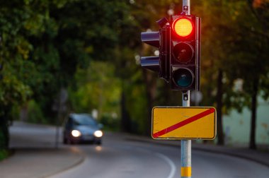 Sonbahar şehrinin odaksız arka planında kırmızı ışığı olan trafik semaforu, yakın plan
