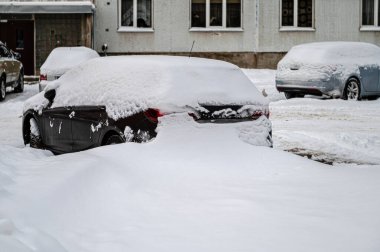 Karla kaplı araçlar bir apartmanın avlusundaki otoparkta.