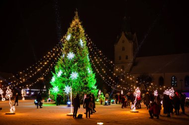 Dobele, Letonya - 4 Aralık 2022 Geceleri, Noel ağacının yakınındaki insanlar ışık ve süslemelerle süslenir.